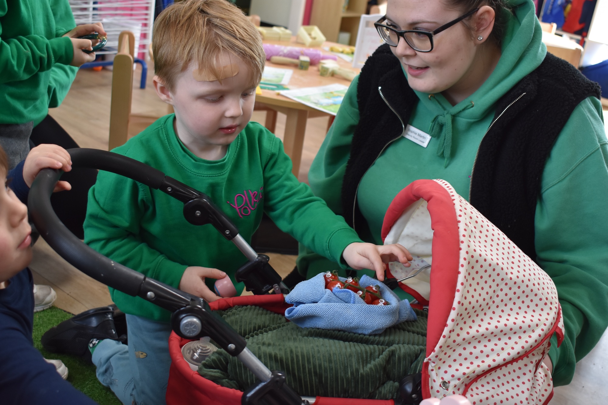 A woman, with some young boys, in an early years setting, showing them the Let's Grow vegetable babies, in a stroller.