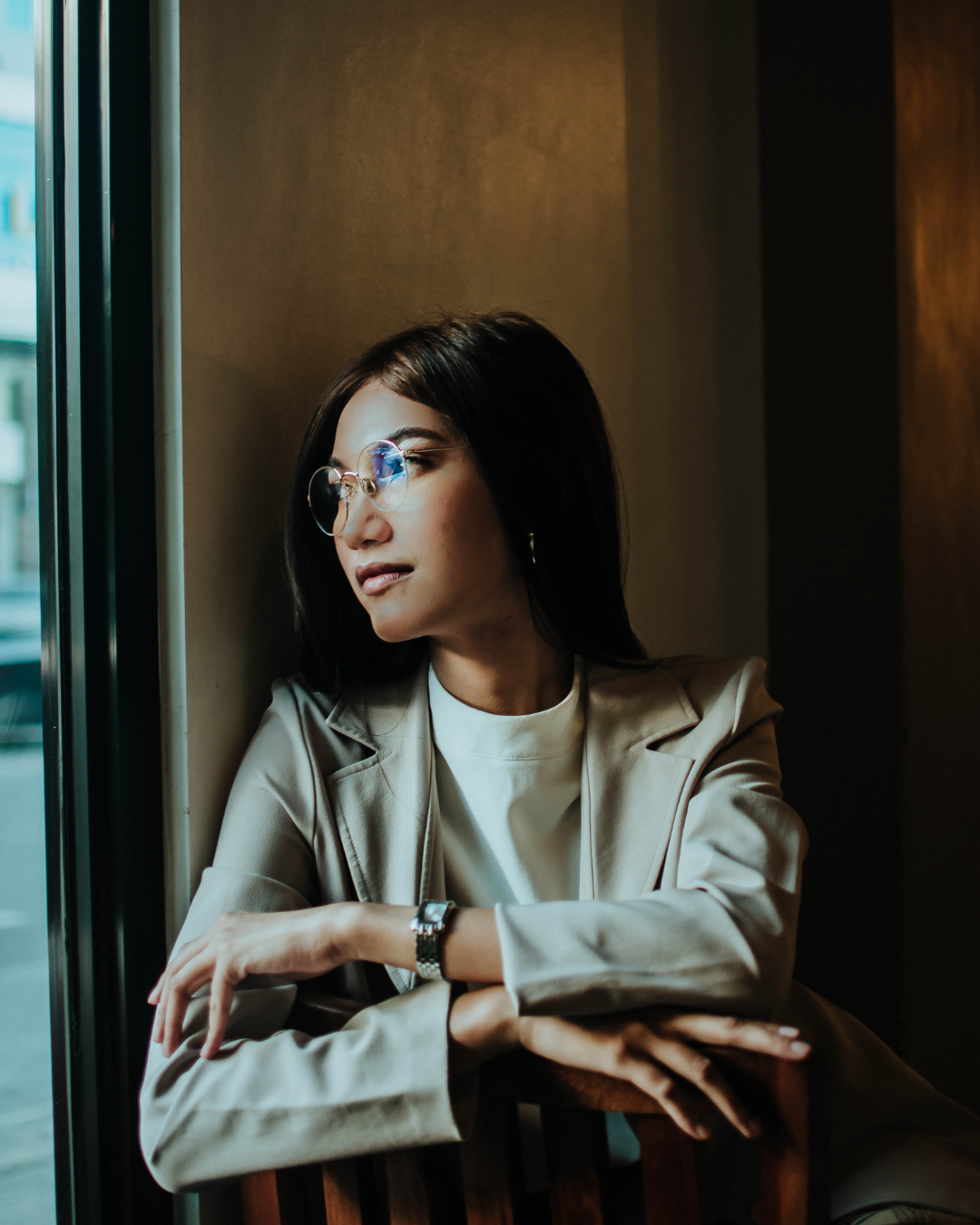A woman in a dark room looking out of a bright window.