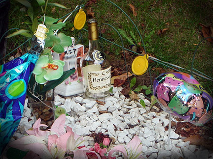 A gravesite decorated with a balloon and a bottle of Hennessy.