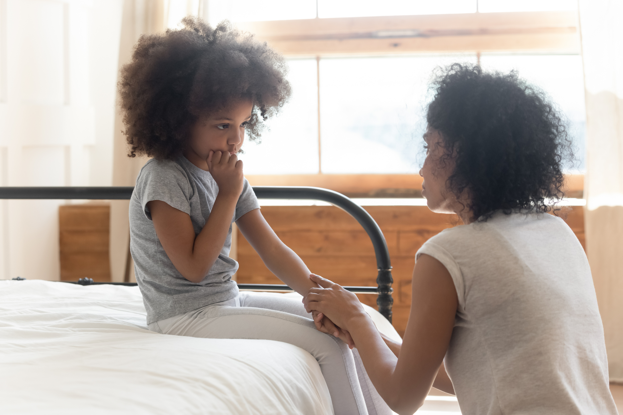 Mother comforting young child sitting on a bed