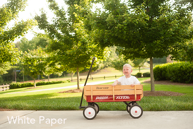 Child wearing a white shirt sitting in a wagon crying.
