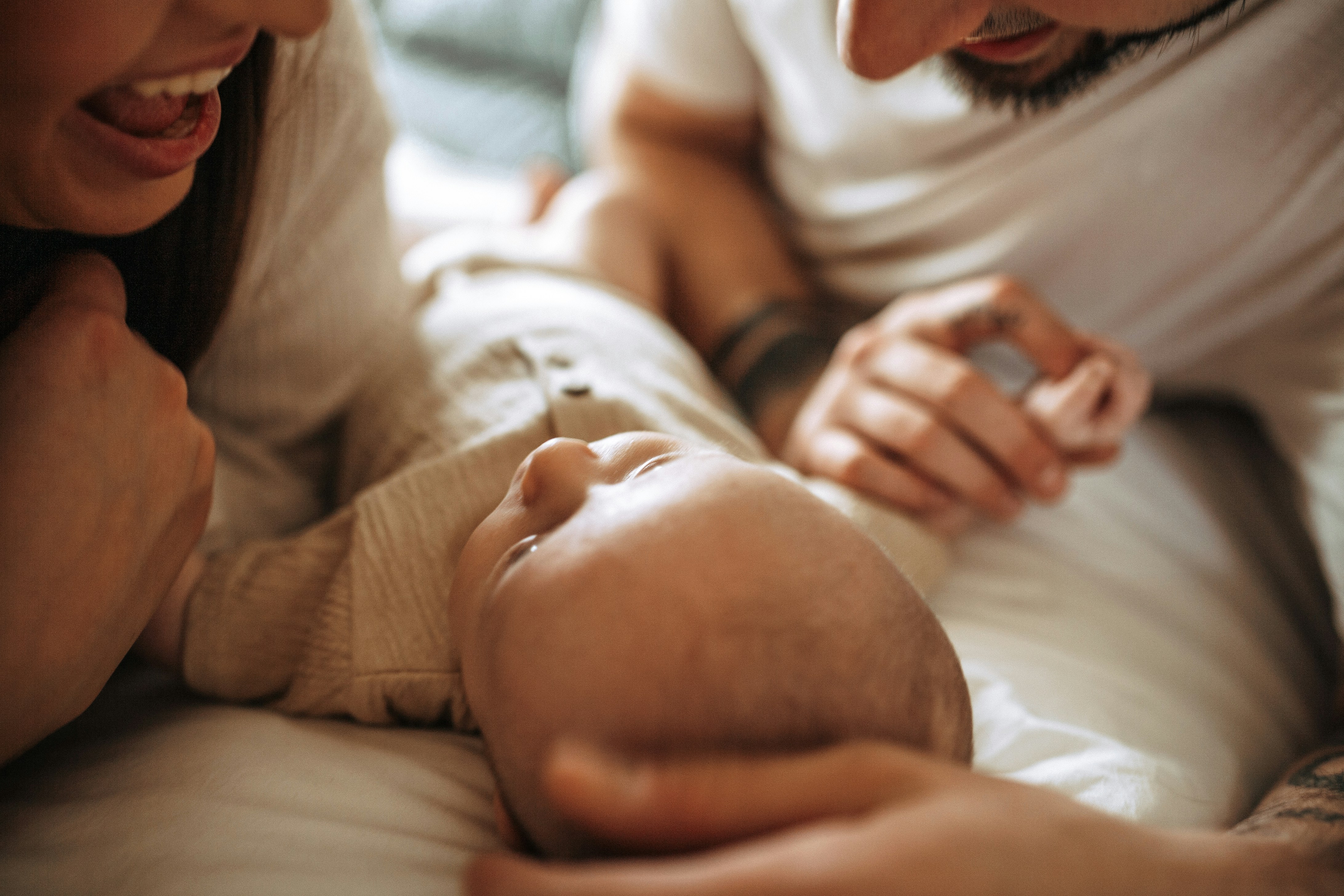 2 parents, each holding one of babies hands, while they all lay on the bed together