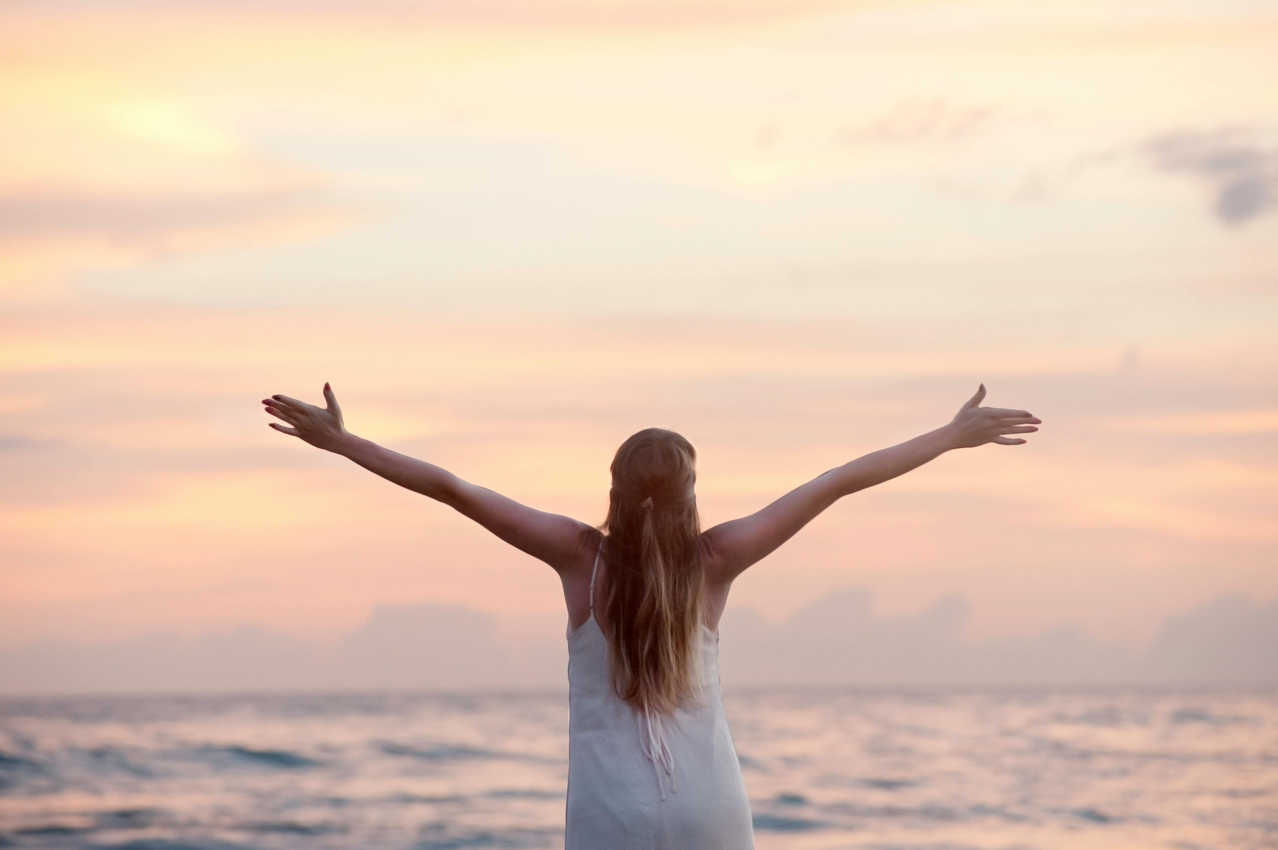 women standing before a shore sunset, arms up wide