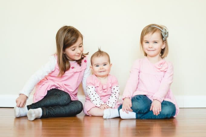 Three children wearing pink sitting on the floor all smiling with correct white balance.