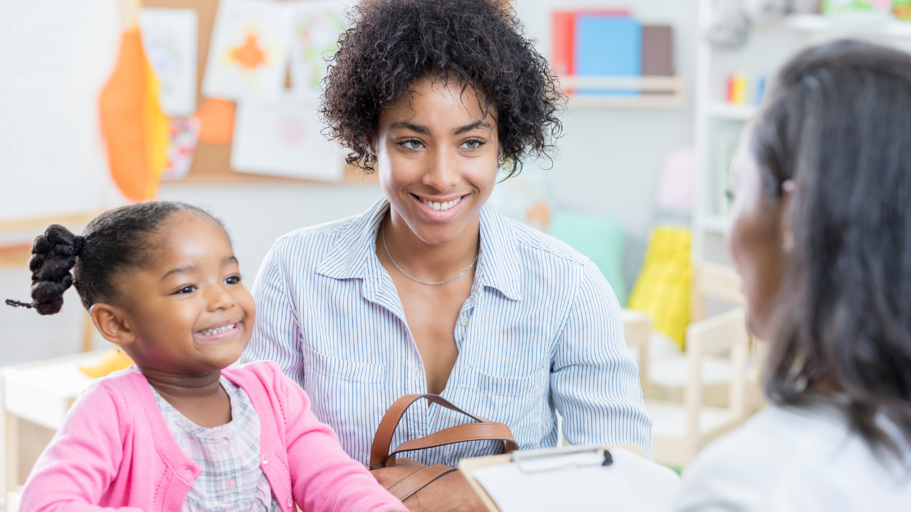 A mother, with her early years daughter, listening to the EYFS teacher sharing the details of the child's learning progress.