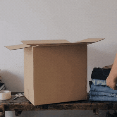 Personne rangeant des vêtements dans un carton de déménagement pour illustrer la technique du faux déménagement pour trier sa maison.