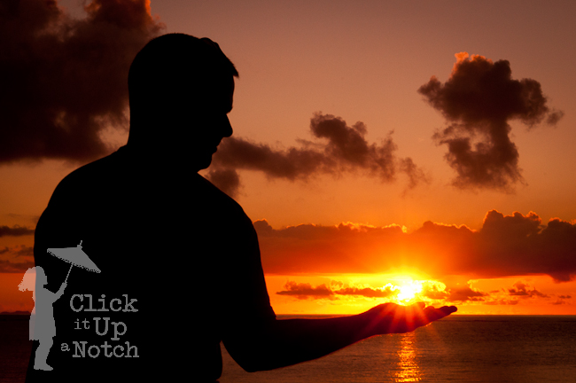 A sunset silhouette of a man holding out his hand to hold the sun that is in a starburst effect.