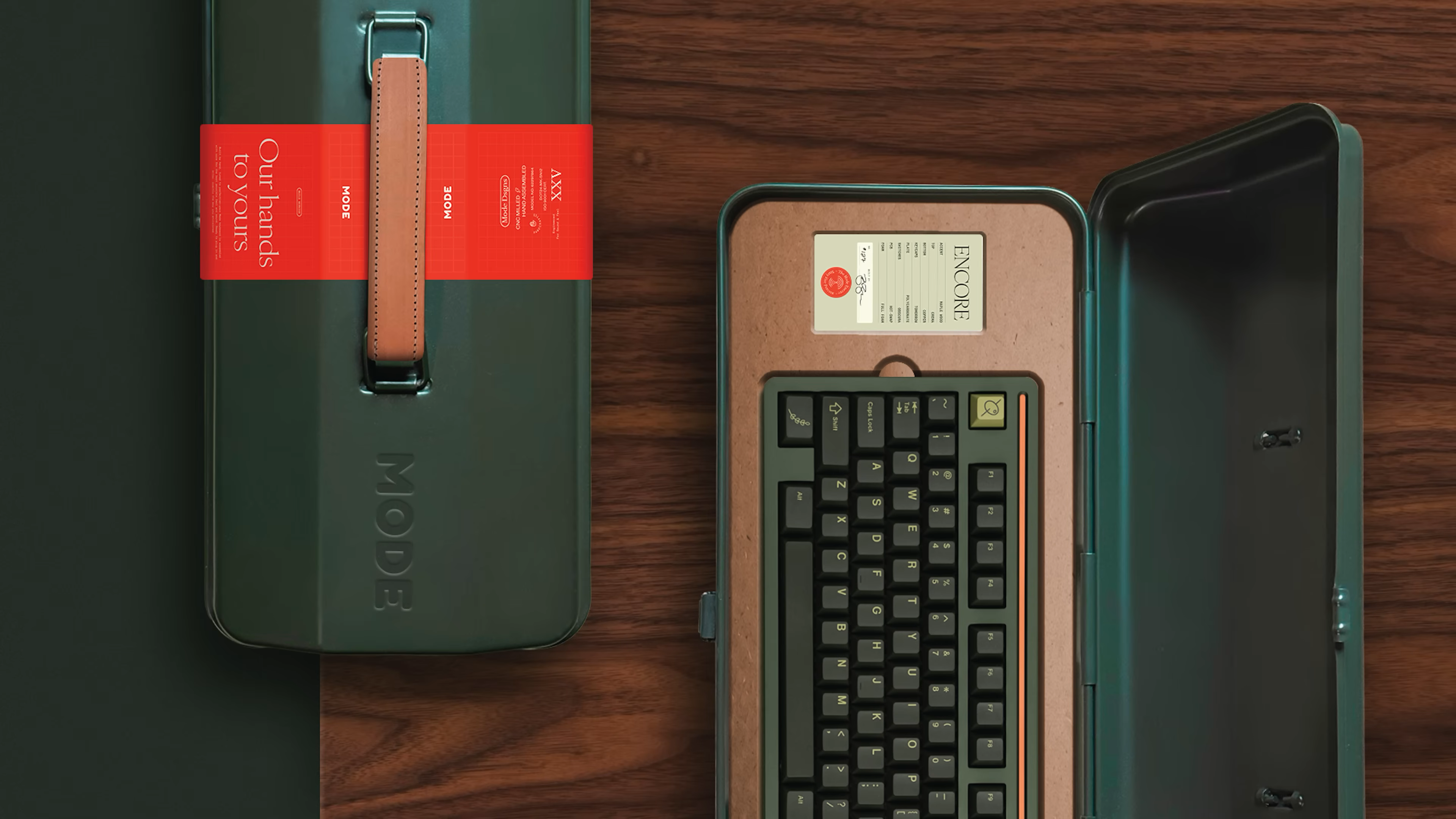 Mode’s green keyboard case with signature handle and red “Our hands to yours” band, shown next to a custom-assembled Encore keyboard with a detailed inspection card—capturing the unboxing and first impressions focus of the brand’s new identity, as explored in the video.