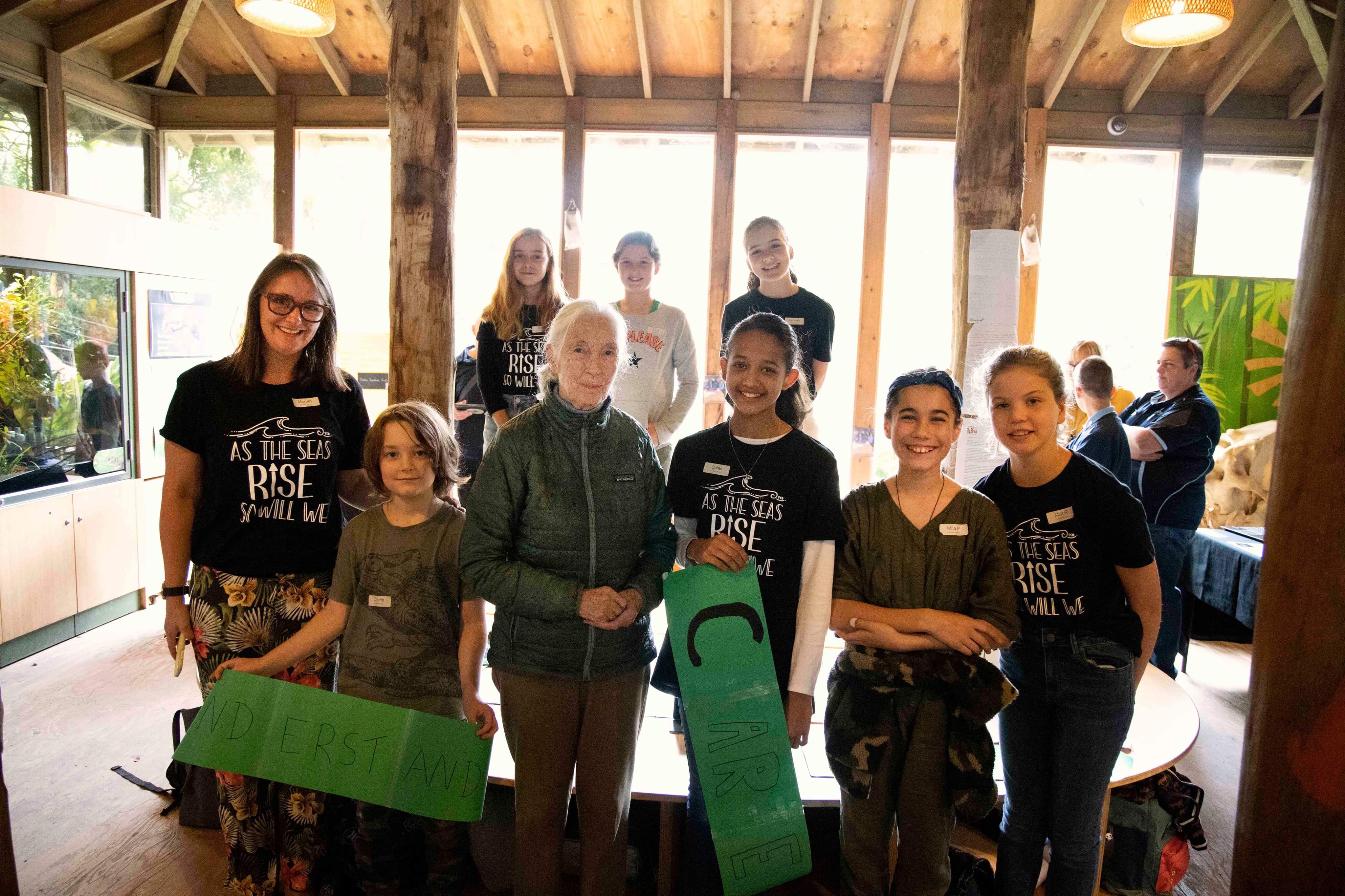A group of students standing in a line holding posters next to Dr Jane Goodall. 