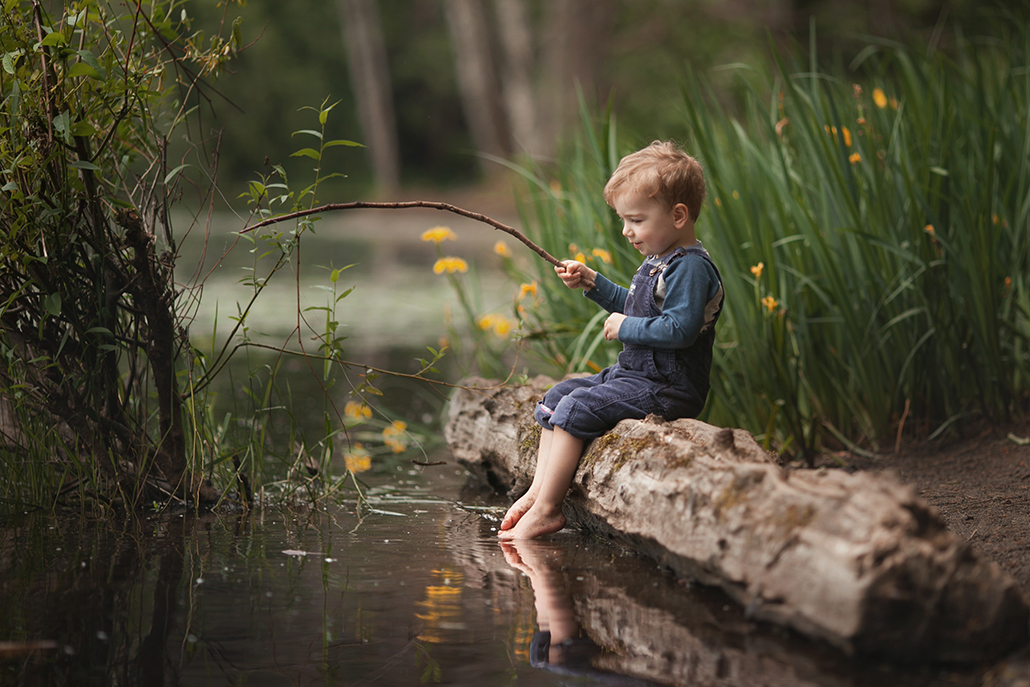 boy sitting on log fishing with stick with log as leading line