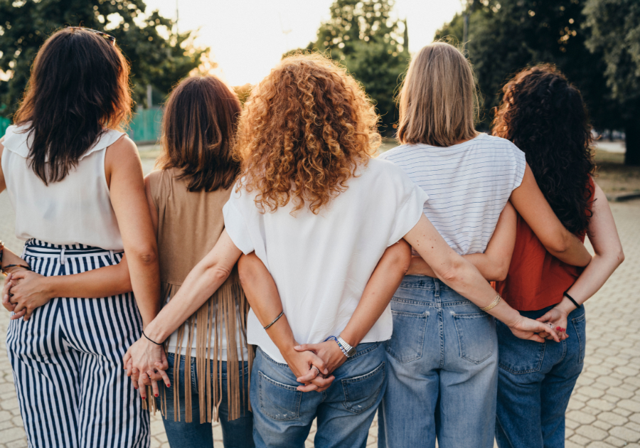 A group of women standing together with their arms around each other to signify unity.