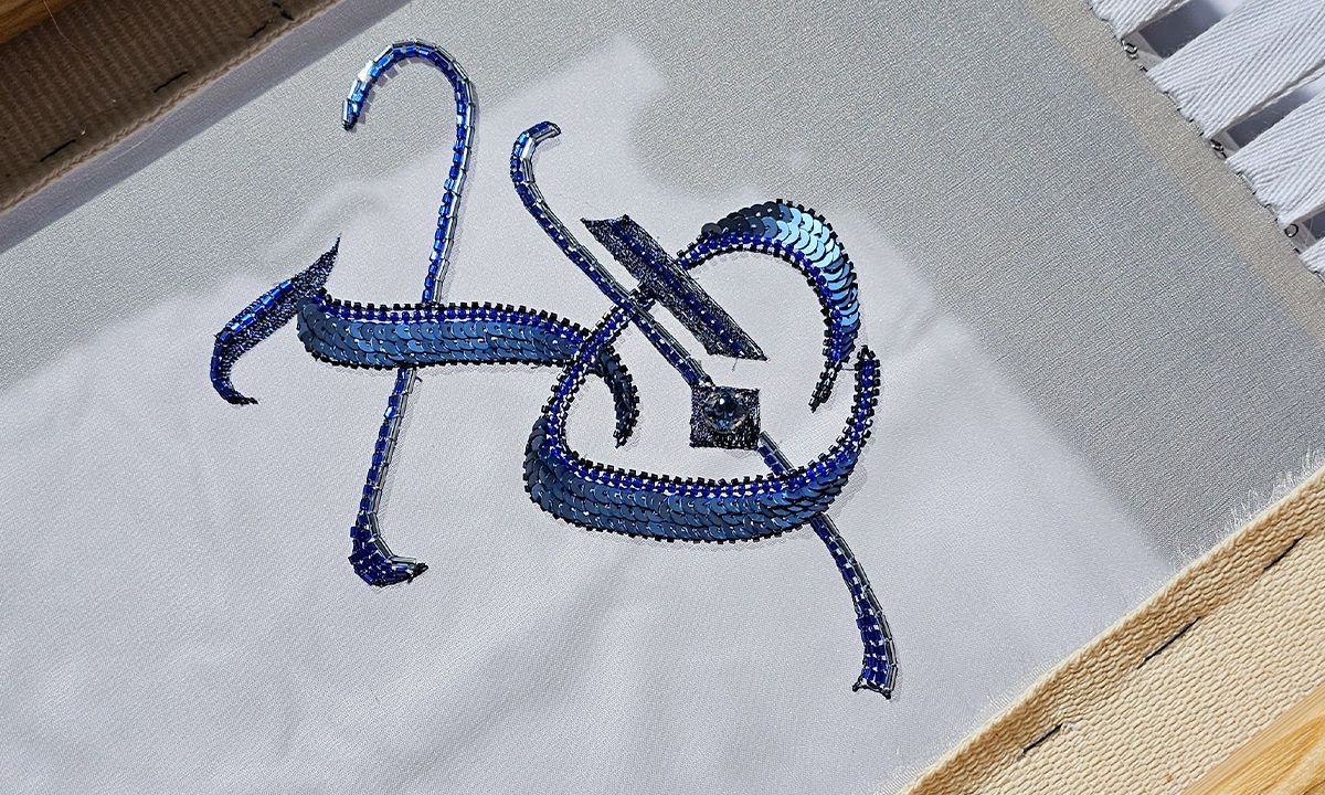 Close-up of Luneville embroidery XO design showing structured sequin lines, beadwork, and precise tambour stitching on silk organza