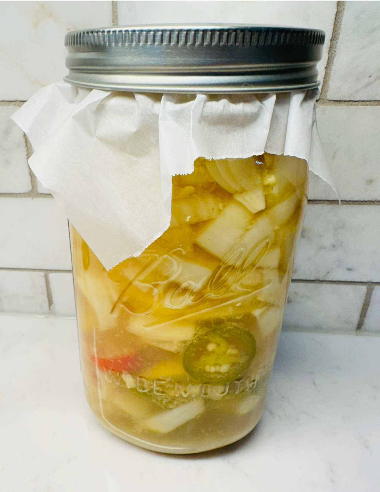 A clear glass jar filled with homemade fire cider, showcasing the vibrant colors of garlic, ginger, and hot peppers infused in apple cider vinegar, placed on a quartz countertop.