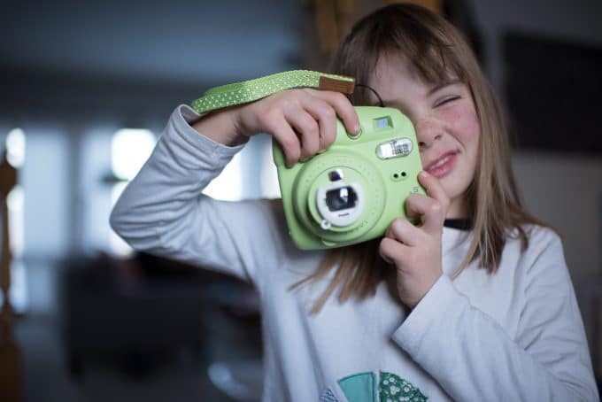 Child holding green camera making a silly face example of  creative photography for kids.