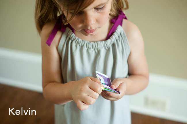 Child holding candy in a grey dress.