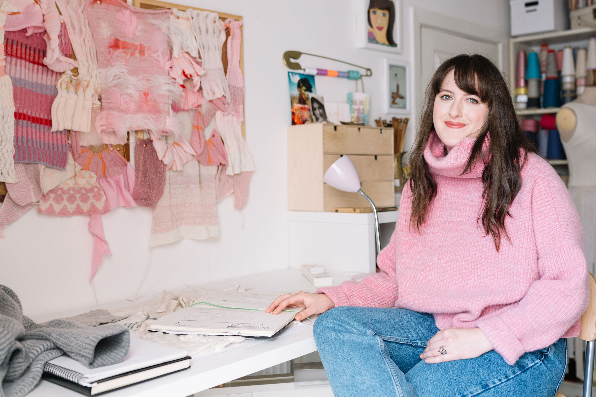 Amber Hards sitting in her studio surrounded by knitting machine fabric swatches and sketchbooks