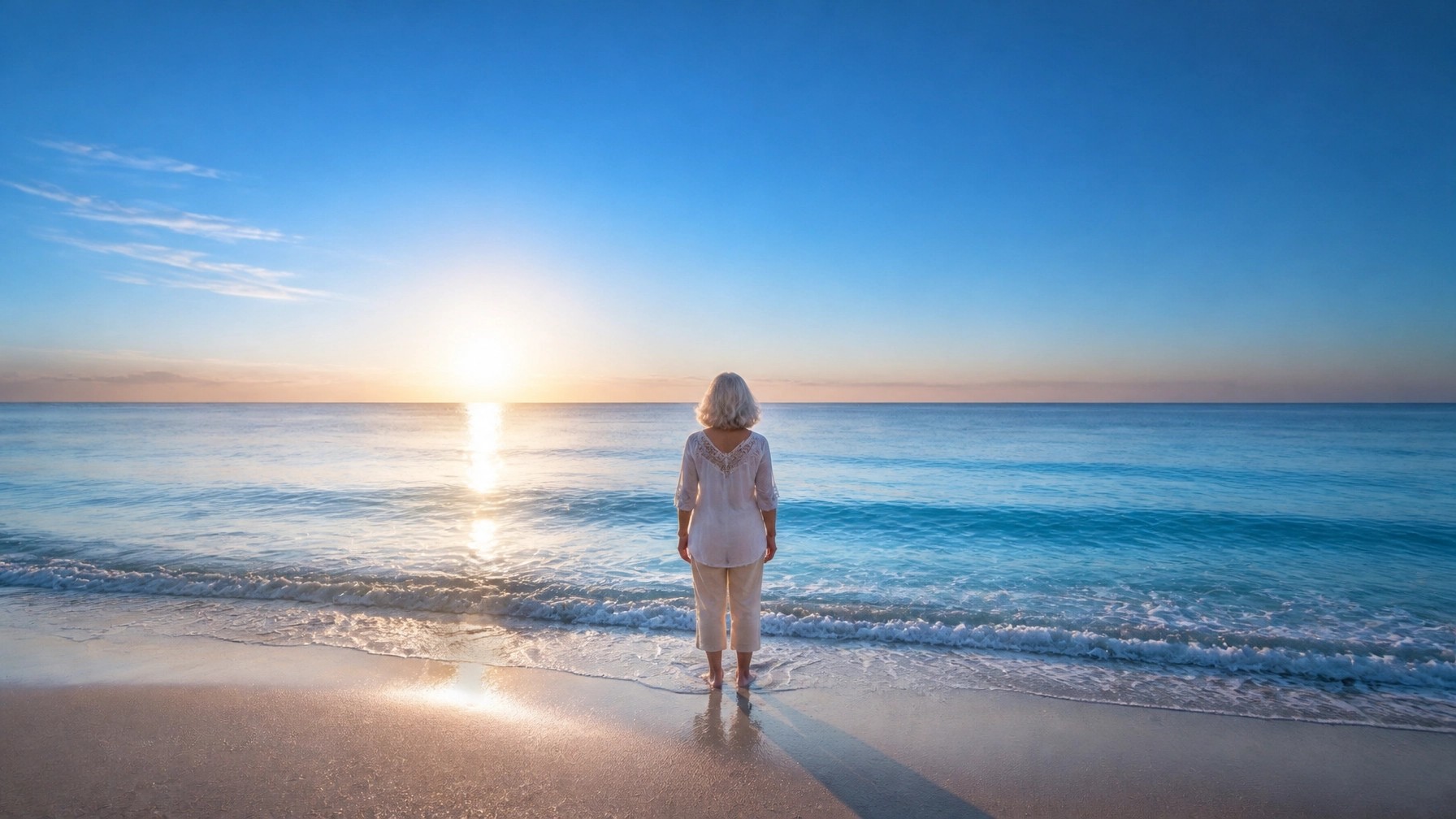 A mature woman standing at the edge of a calm, deep blue ocean, gazing into the first light of a serene sunrise.