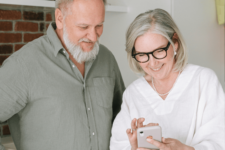 Couple de seniors regardant un smartphone ensemble, échangeant sur l’organisation de leur maison pour rester chez eux durablement