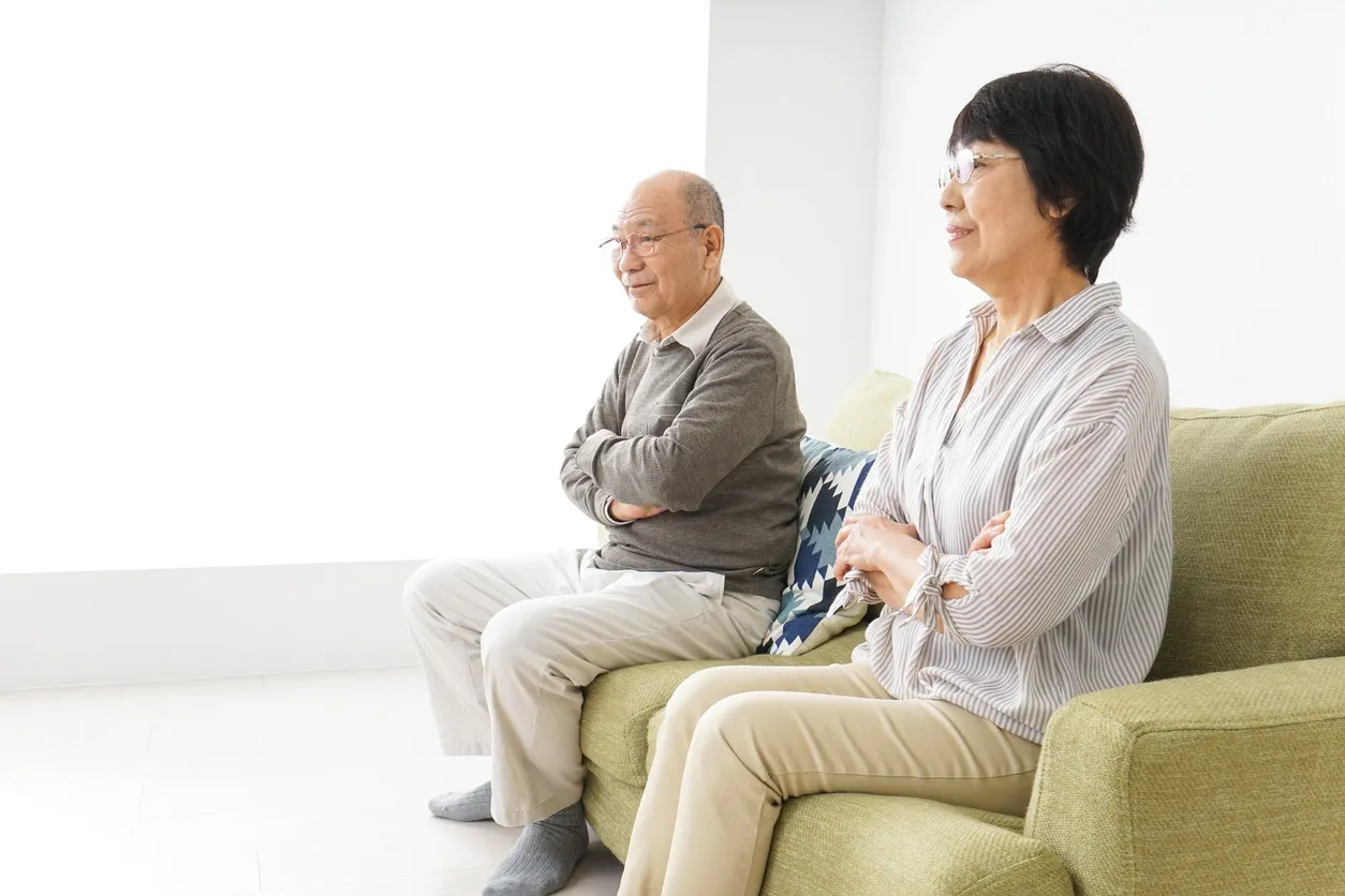 Older couple sitting on a couch with folded arms, appearing emotionally distant, representing the role of nonverbal cues in relationship communication.