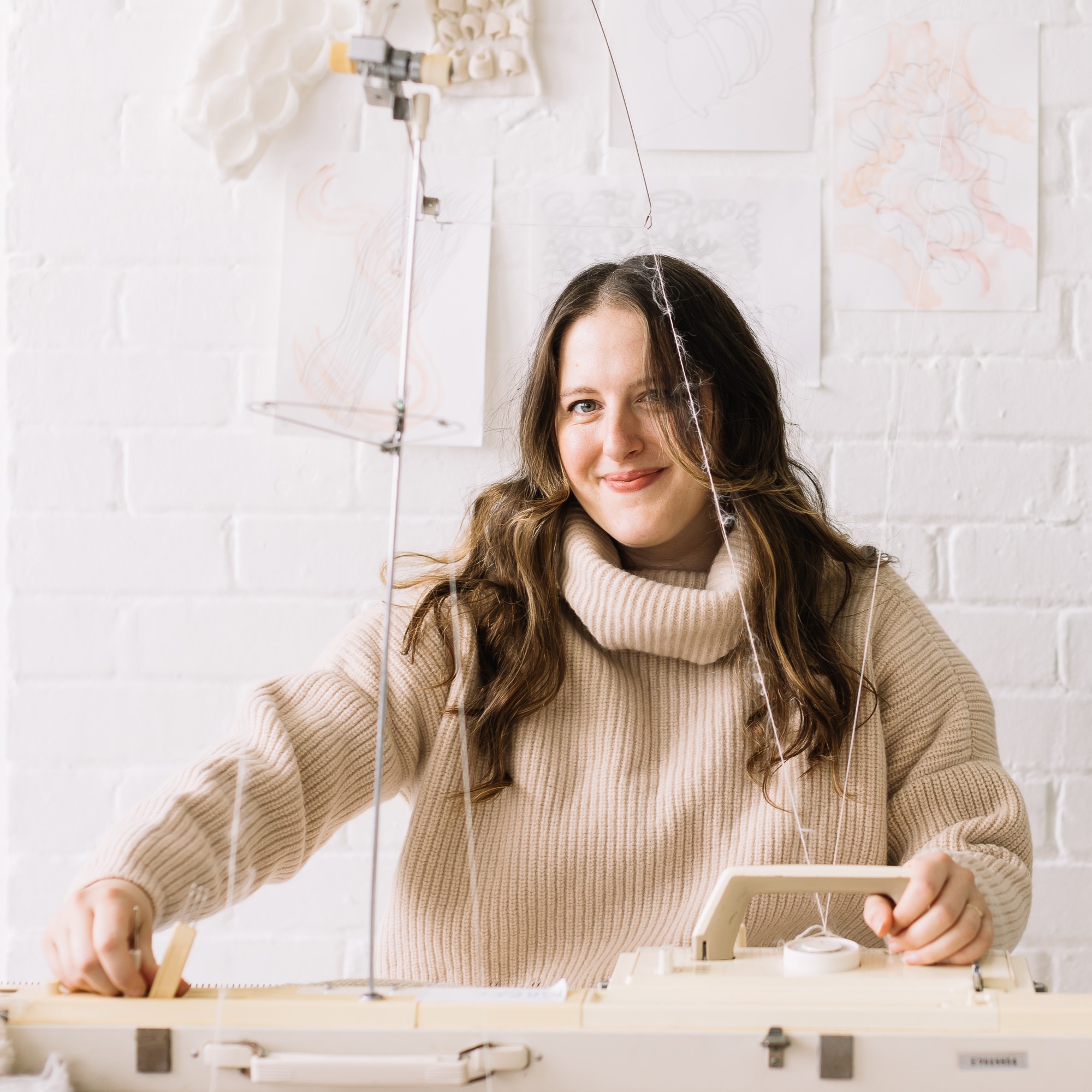 Amber Hards sitting in a chair in front of her knitting machine
