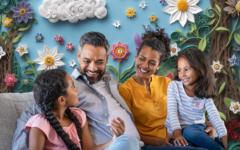 Smiling family of four sitting on a couch and talking together, with a whimsical paper-quilled floral background, illustrating joyful parent-child connection through storytelling.
