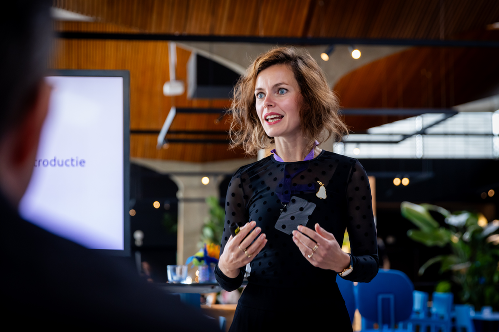 Liza staat voor een groep mensen uitleg te geven.