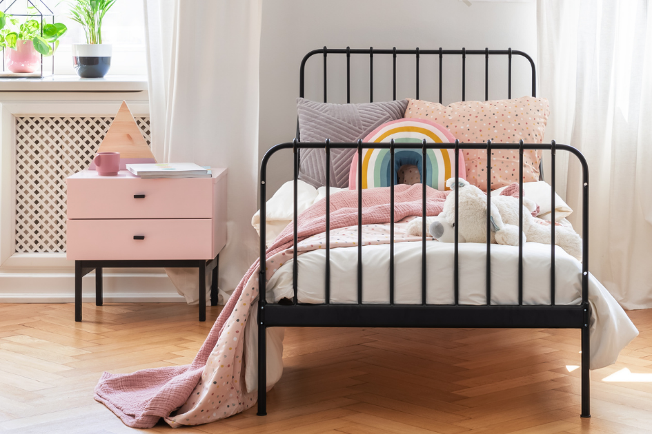 Chambre d’enfant lumineuse avec lit, coussins colorés, peluche et table de chevet, illustrant un espace de sommeil apaisé et organisé.