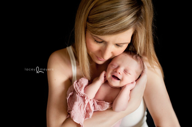 mother in white tank top holding baby in a pink wrap for newborn photography shoot.