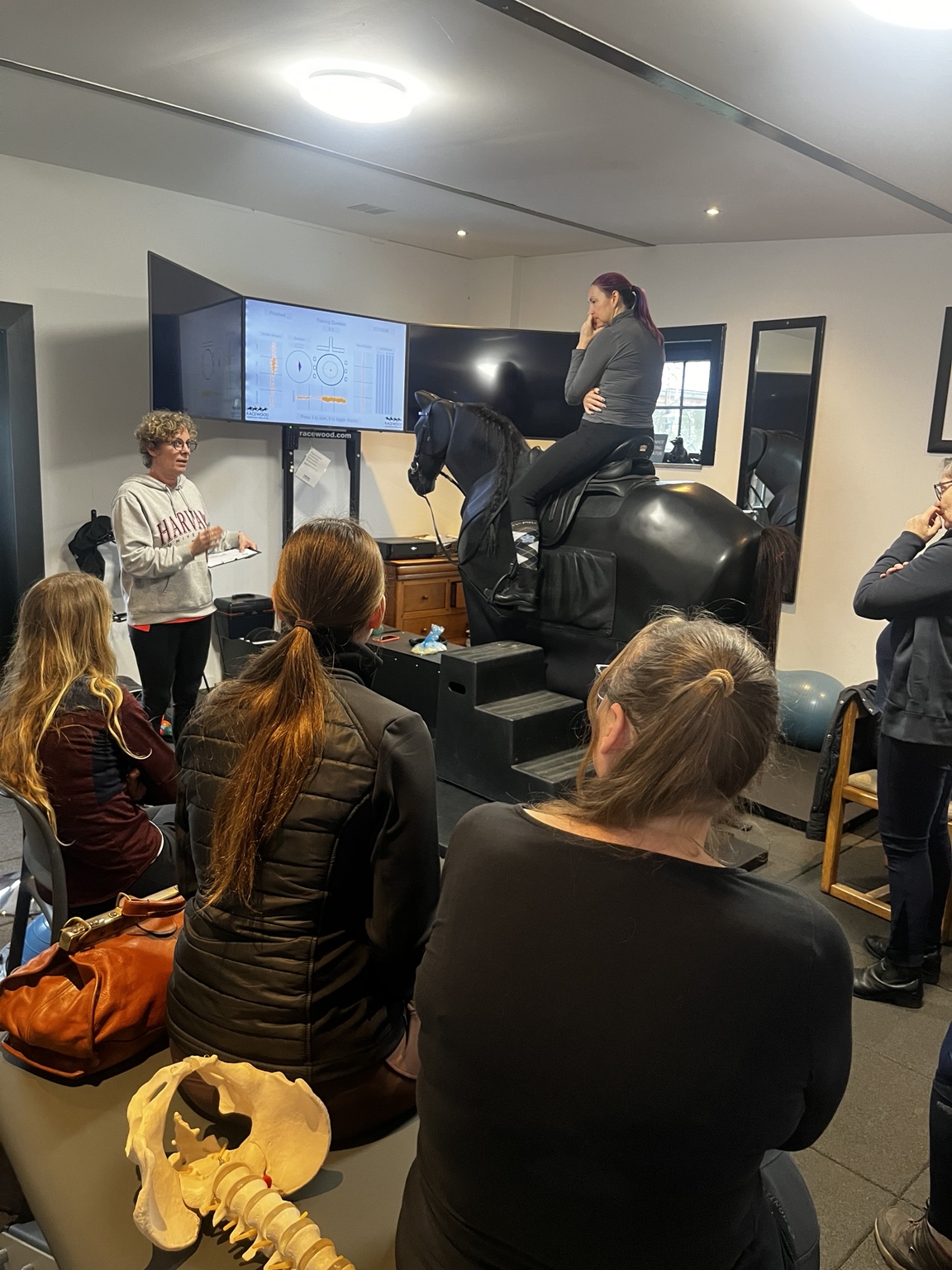 Nadia Molenaers bespreekt de houding van een ruiter op de paardrijsimulator terwijl deelnemers en meetgegevens meekijken