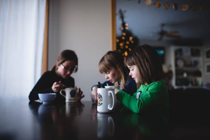 photo of 3 children at a table with mugs and the christmas tree in the background.