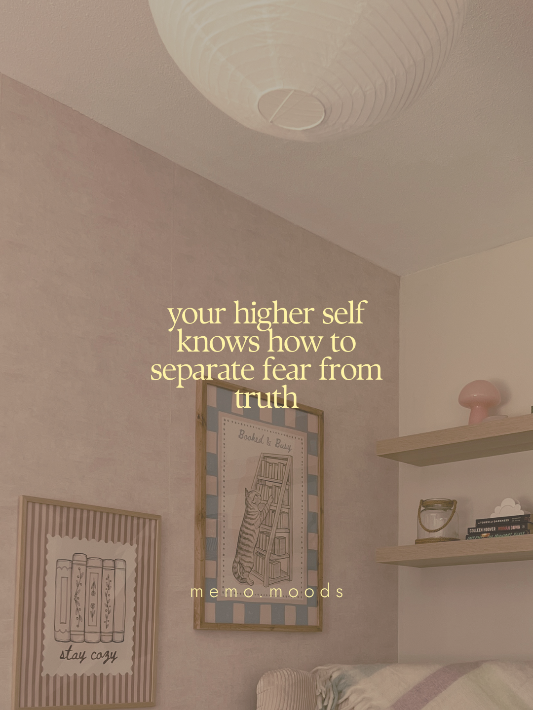 Quote graphic over a cozy warm-toned bedroom corner with a paper lantern ceiling light, cute wall art prints including a "stay cozy" books poster and a cat climbing a bookshelf poster, and a shelf with books and a pink mushroom lamp. Text reads: "your higher self knows how to separate fear from truth." by memo.moods.