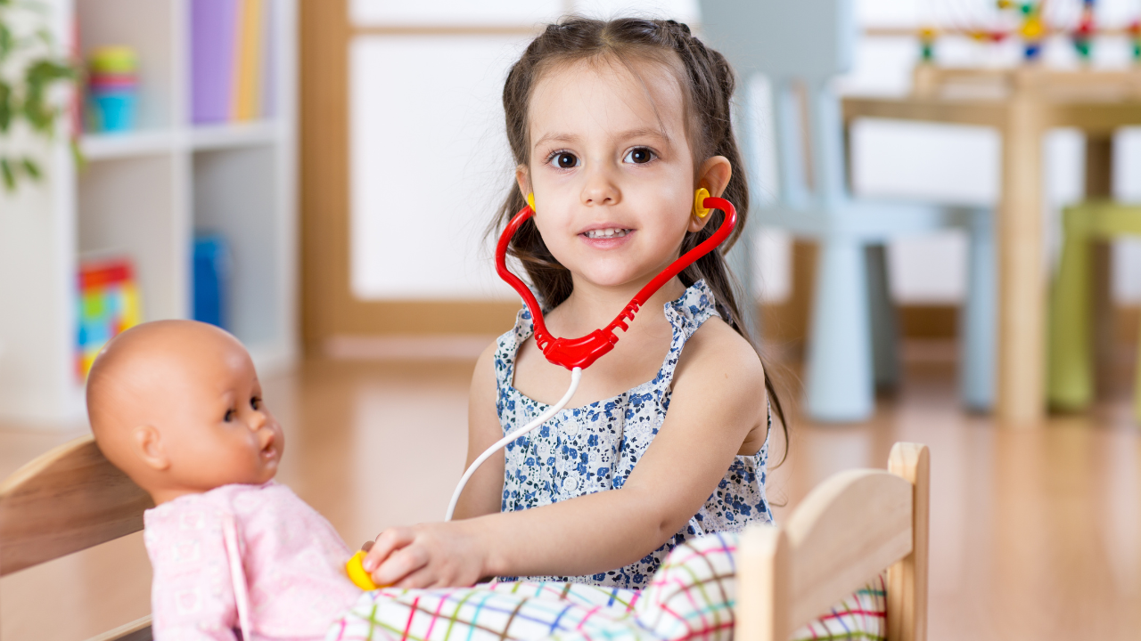 A young child exploring imaginative play, being a pretend doctor to a baby doll, in a colourful playroom setting.