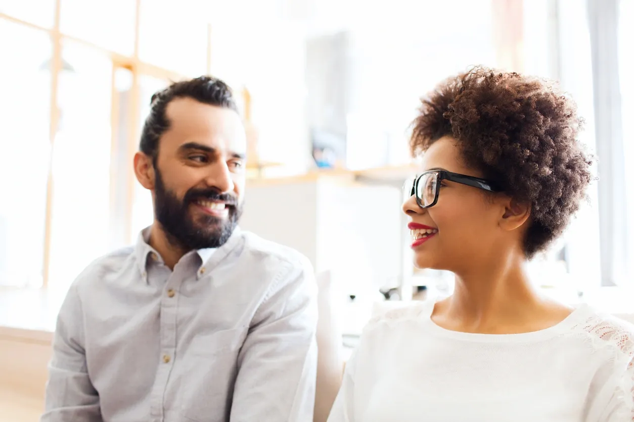 A couple smiling at each other and talking closely, showing engagement, eye contact, and emotional connection during a conversation.
