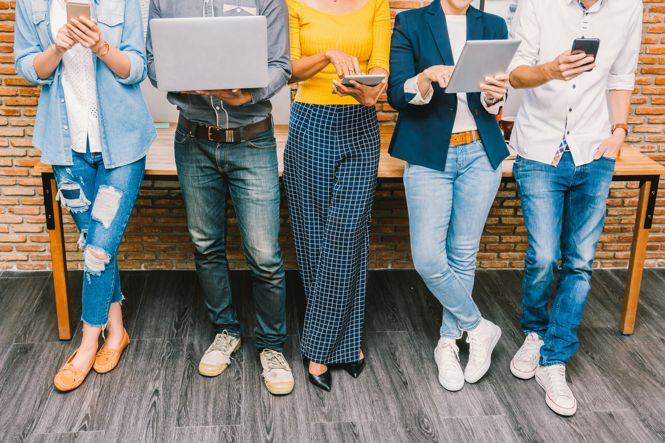Five people holding laptops or phones, some in jeans and one in dressy pants and heels
