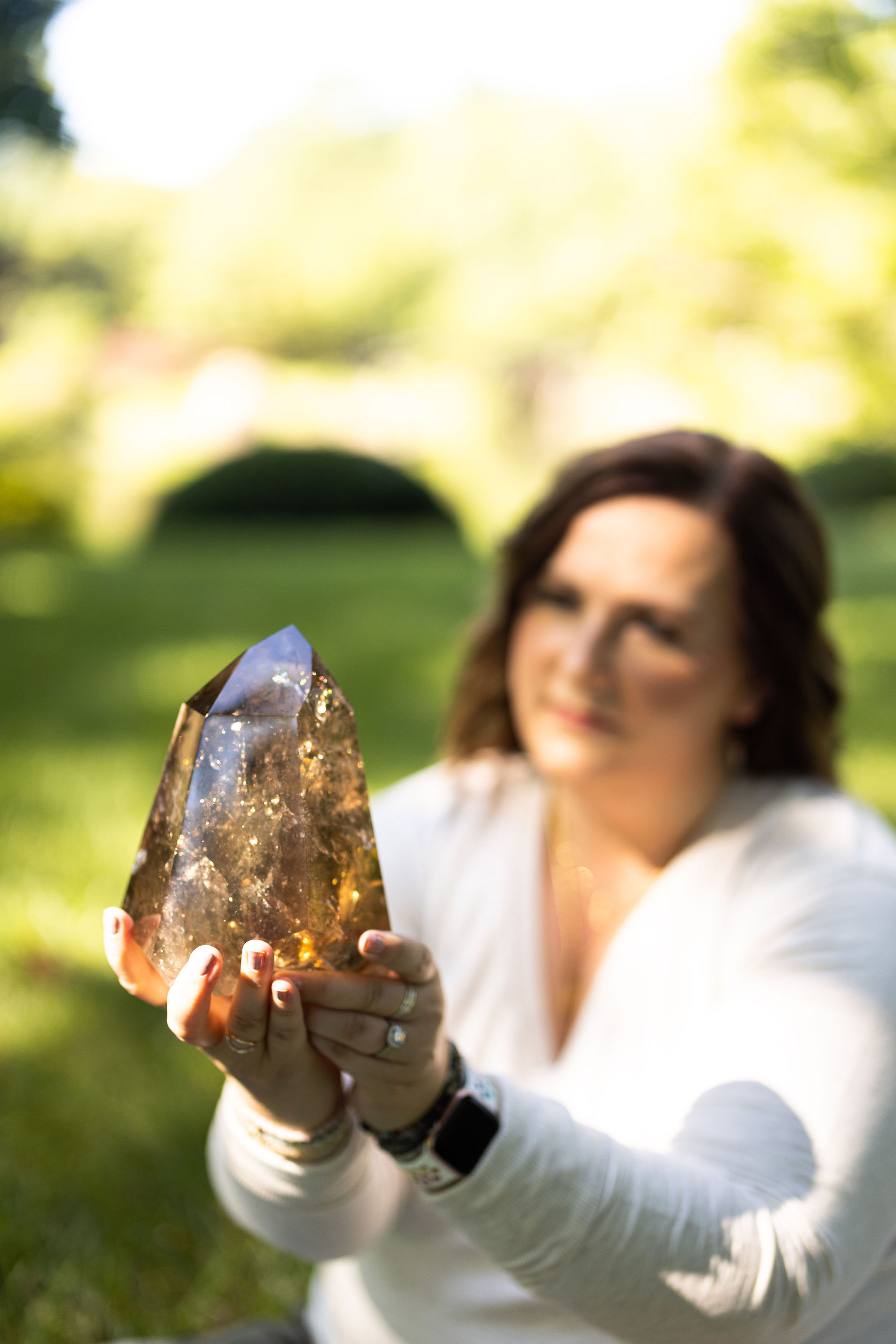 A woman holds a large Smoky Quartz from Brazil in a sunbeam. The landscape and the woman are out of focus.