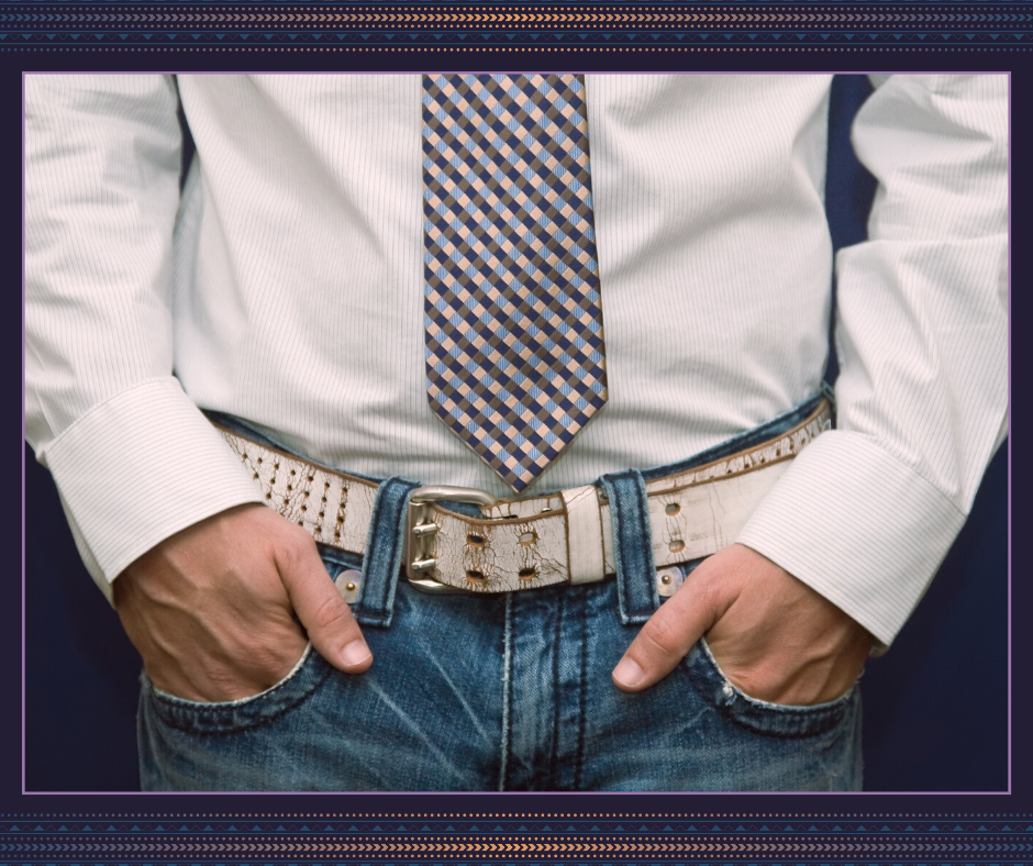 A person in jeans, shirt and tie, with hands in pockets, thumbs out.