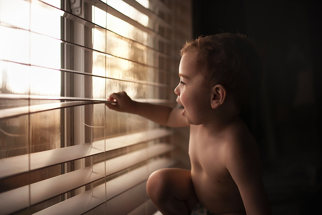 child looking out blinds with blinds acting as a leading line