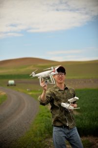 Zhou Tang holding a drone in a field.