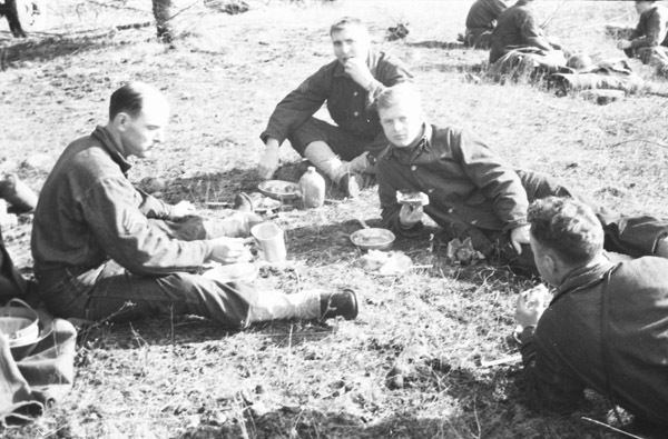 A group of four soldiers sitting and laying on the ground eating food.