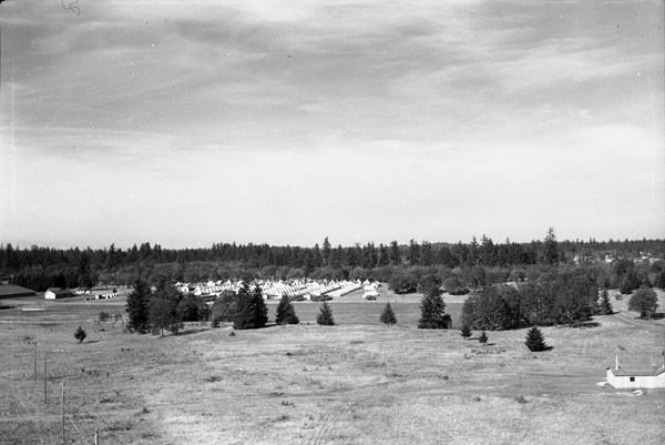 A semi-permanent military camp made up of many tents along a dirt road in a wooded clearing.  The picture was taken from far out of the camp.
