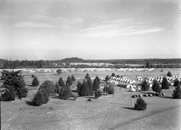An view from on high and at a distance of a semi-permanent military camp in a wooded clearing.