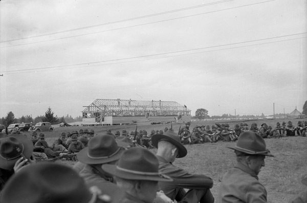 Soldiers sitting on the grass in a semicircle. A few are seen holding rifles.