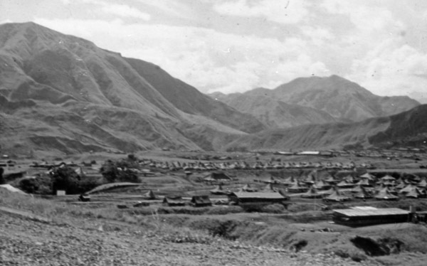 A large military tent camp set in a low area surrounded by mountains.