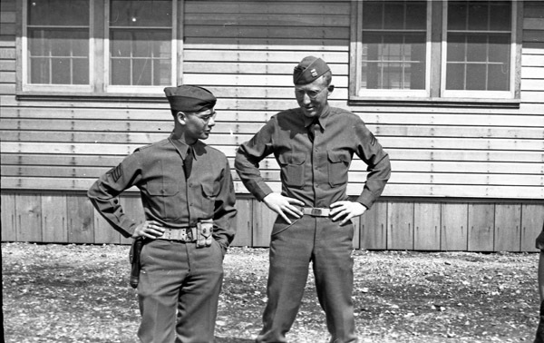 Two soldiers facing the camera and talking with one another, while having their hands on their hips in a relaxed pose.