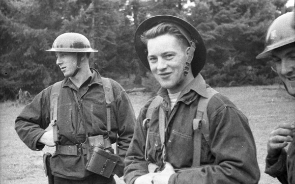 Three soldiers in uniforms standing in front of a tree line.  The center man is looking at the camera, while the others look in other directions.