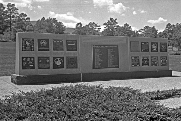 An outdoor memorial, with a central larger plaque and flanked by two sets of eight smaller plaques on both sides of the central one.