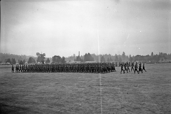 A long line of over a hundred soldiers walking in formation. A tent camp can be seen in the background.