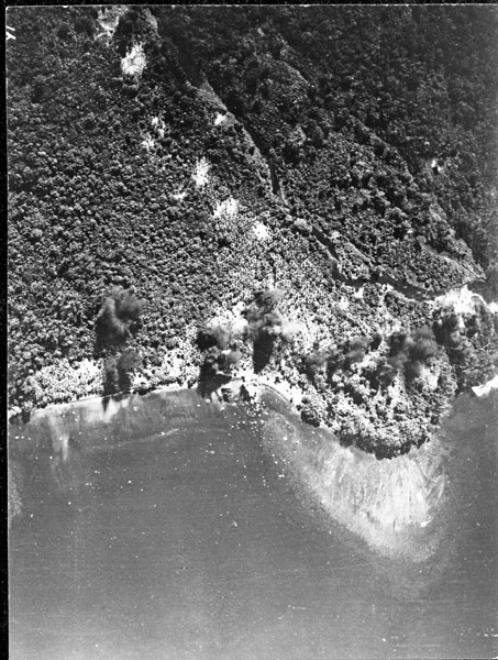 Bombs landing and exploding on a shoreline as seen from the air.