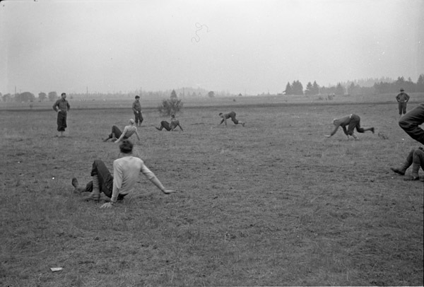 A group of men in a field crawling on all fours or doing crab walks while others stand and watch.