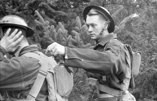 Two soldiers, with the one on the left poking or tickling the soldier on the right on their neck with a stick.  The man on the right is holding up their hand to their neck.